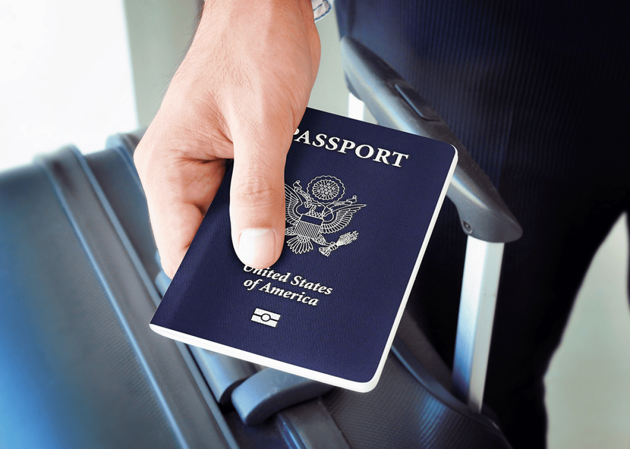 Hand holding U.S. passport and wheeling a suitcase.
