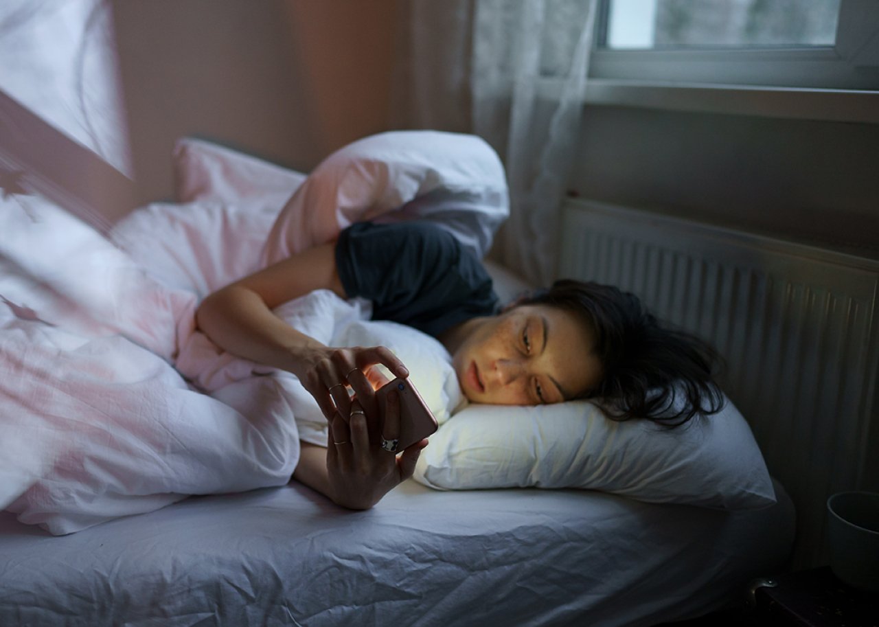 Young woman lying on her bed at home scrolling on social media.